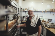 Baker standing next to a pizza oven in his bakery