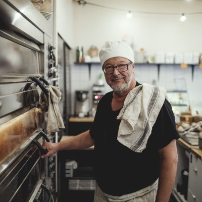 Baker standing next to a pizza oven in his bakery